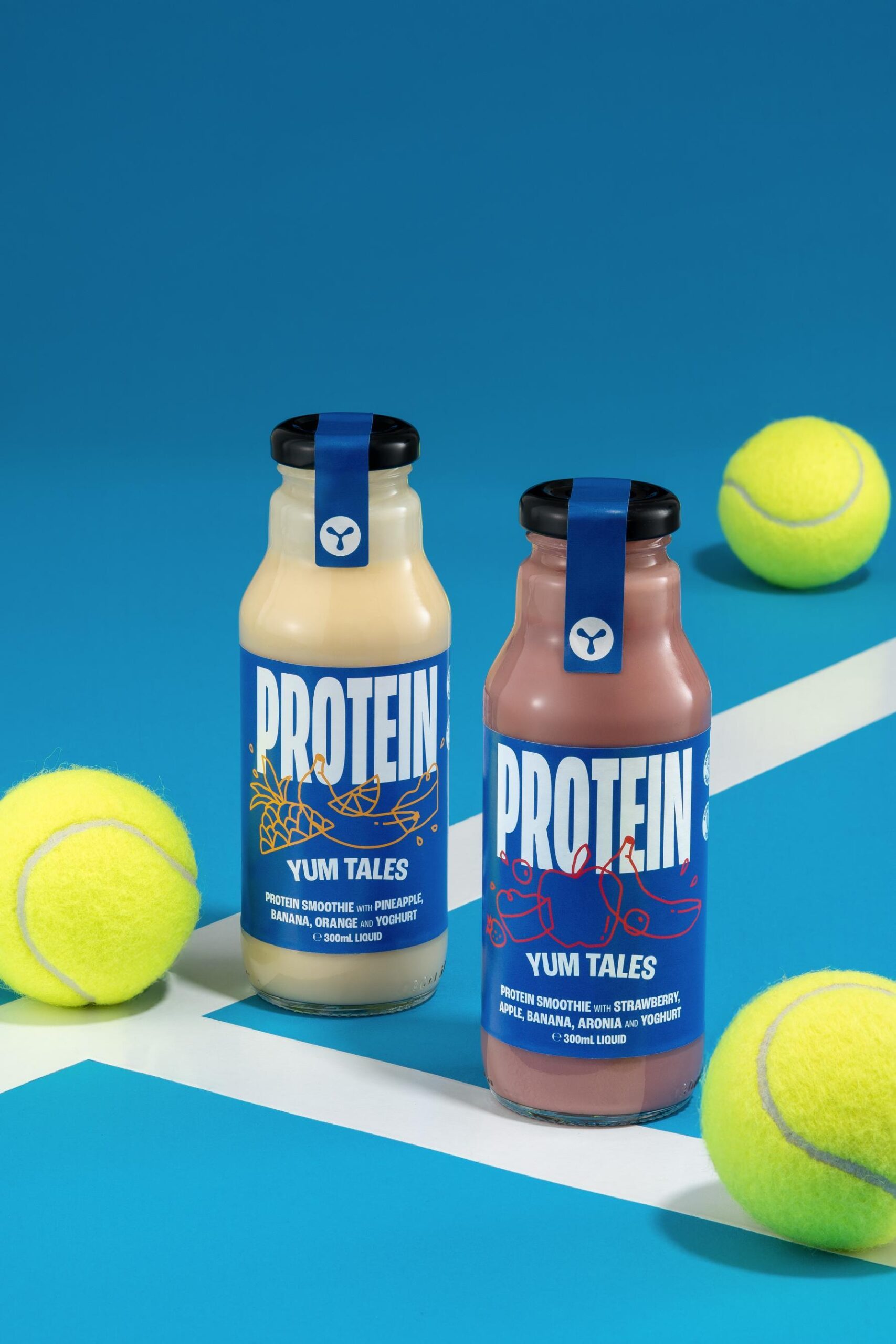 Protein Smoothies Pinapple and Strawberry sitting on tennnis court surrounded by tennis balls